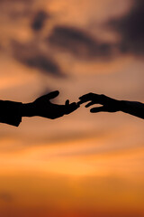 Valentine day. Silhouette of hands of woman and man reaching each other, touching fingers with tenderness on orange sunset sky background. Helping hands, save and support people concept. Friendship