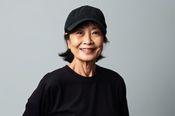 Medium shot portrait of a Chinese woman in her 60s in a white background wearing a cool cap or hat - obrazy, fototapety, plakaty
