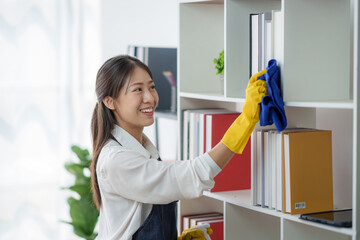 Asian woman cleaning bookshelves inside house