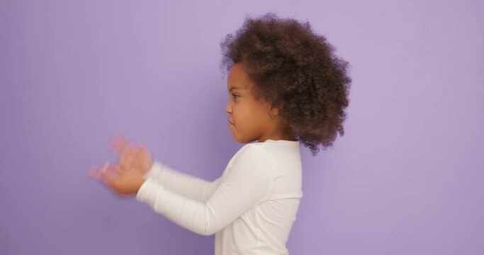 cute funny naughty African American child girl making silly faces. female kid having fun, smiling, dancing, shows pistols with hands, dancing, jumping Slow motion isolated purple background