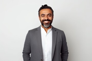 Portrait of a smiling bearded Indian businessman standing against white background.