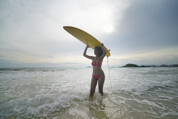 Front view of African american woman with surfboard at beach in the sunshine