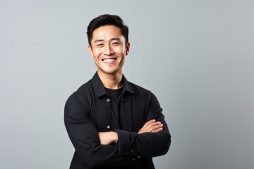 Fototapeta premium Portrait of a happy young asian man standing with arms crossed over gray background