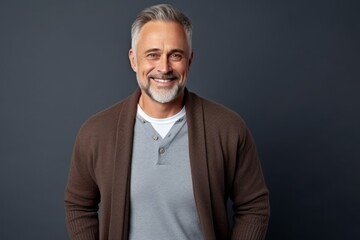 Obraz premium Portrait of handsome mature man smiling at camera, standing against grey background