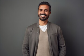 Portrait of a handsome bearded Indian man smiling at the camera while standing against grey background