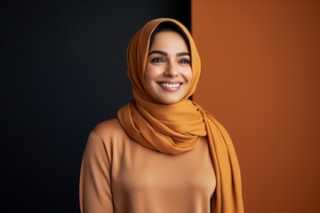 smiling muslim woman in hijab looking at camera isolated on black and orange