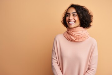 Obraz premium Portrait of a smiling young woman in sweater and scarf looking at camera isolated over beige background