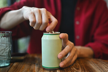 Close up with a Young Asian man's hands opening a drinking can while sitting at the wooden table - obrazy, fototapety, plakaty