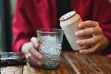 Close up with a Young Asian man's hands holding a soft drink can and glasses with ice in the...