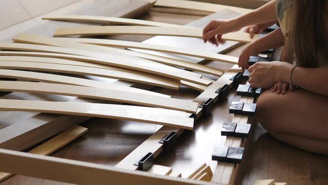 Close up view of mother with kids assembling wooden slats of an orthopedic base of a double bed. Interior structure of furniture. The concept of a single mother. Family activity together.