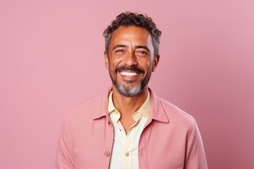 Fototapeta premium Portrait of handsome Indian man smiling at camera while standing against pink background