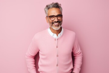 Fototapeta premium Portrait of handsome mature man in glasses looking at camera and smiling while standing against pink background