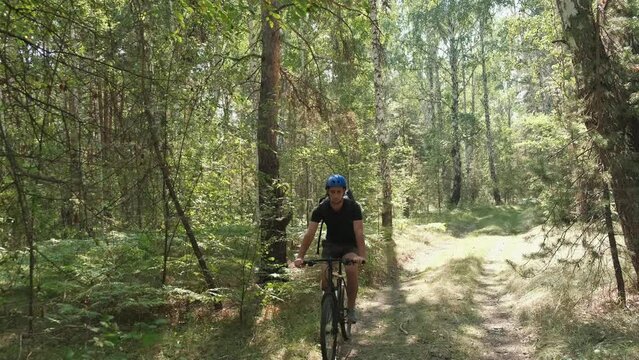 mountain bike.An active lifestyle.A cyclist in a helmet and with a backpack rides a mountain bike and stops to rest and look around in the forest.Slow motion