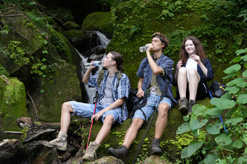 Hikers walking along a trail on a mountain with hiking sticks. Adventure, travel, tourism, hike and people concept. Group of smiling friends with backpacks outdoors.