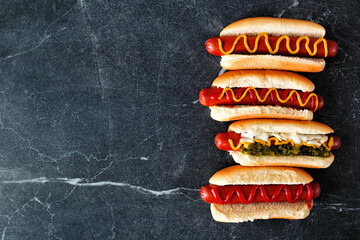 Variety of hot dogs with an assortment of toppings. Top down view side border on a dark stone background.