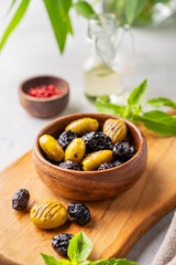 A set of green and black dried olives in bowl on a light background with olive oil and basil close up. The concept of vegetarian healthy snacks