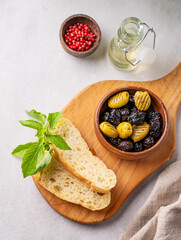 A set of green and black dried olives in bowl  with fresh chiabatta slices on a light background with olive oil and basil close up. The concept of vegetarian healthy snacks.