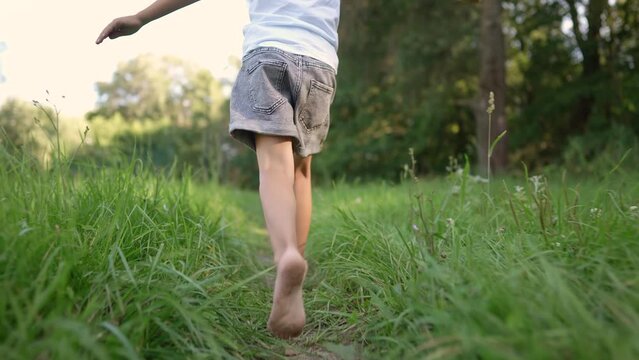 girl running on the grass in the park in summer. happy family childhood dream concept. a little girl with bare feet runs along the green grass in a summer park. child lifestyle running down the path