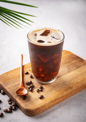 Iced coffee brew in a glass on a wooden board on a light  background with coffee beans and palm leaf. Summer refreshment concept.