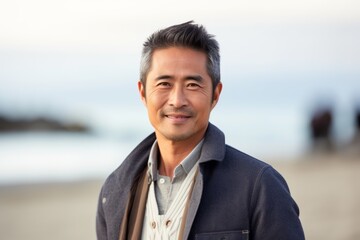 Lifestyle portrait of a Chinese man in his 40s in a beach background wearing a chic cardigan