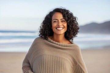 Portrait of smiling young woman standing on beach with arms akimbo