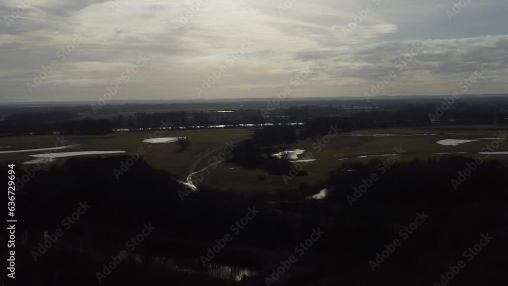 Poster aerial view of vast green fields and trees by a pond with gray cloudy sky on the horizon