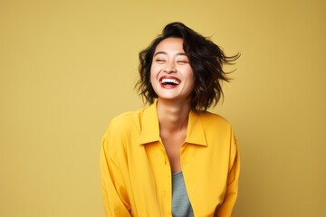 Portrait of a happy young woman laughing isolated over yellow background.