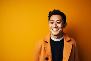 Obraz premium Portrait of a smiling young asian man in coat on yellow background