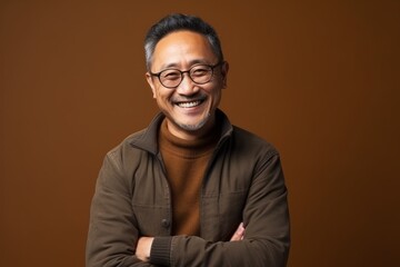 Fototapeta premium Portrait of a smiling asian man wearing glasses against brown background