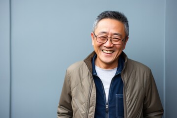 Portrait of happy mature Asian man with eyeglasses against blue background