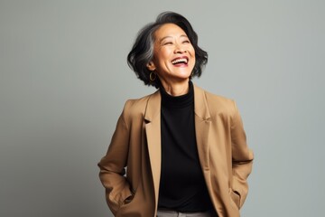 Portrait of a happy mature asian businesswoman laughing over grey background
