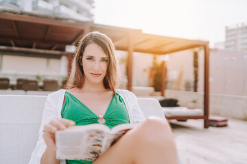 Chica joven en traje de baño leyendo libro en cama balinesa en piscina de hotel de lujo