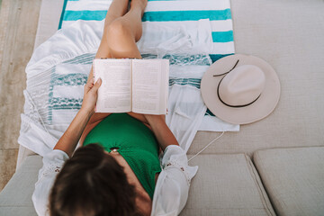 Chica joven en traje de baño leyendo libro en cama balinesa en piscina de hotel de lujo