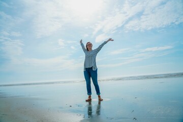Obraz premium woman with arms outstretched on beach standing near water with sky in background