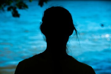Young adult with dark hair stands in front of an outdoor landscape with a river in