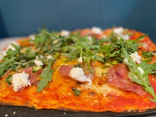 Pizza Calabrese on a rectangular base with beef salami, green chilies, jalapeno peppers, mozzarella, bocconcini, rocket, pesto and parmesan.
