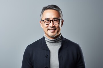 Portrait of a middle-aged Asian man wearing glasses and a sweater on a gray background