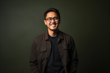 Obraz premium Portrait of a smiling young asian man wearing glasses against green background