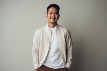 Portrait of a handsome young asian man looking at camera and smiling while standing against grey background