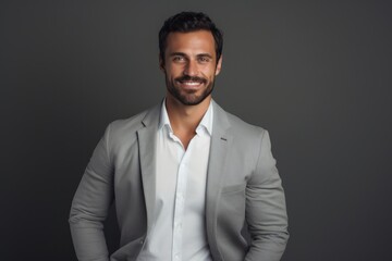Portrait of a handsome young businessman smiling at camera while standing against grey background