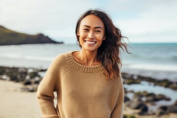Fototapeta premium Portrait of a smiling young woman standing on the beach at autumn day