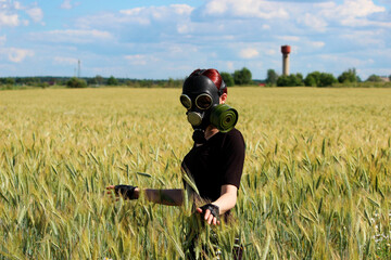 young girl stands in a gas mask in the middle of a wheat field. August. Environmental pollution concept