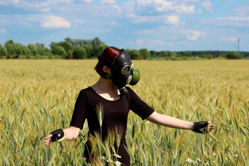 young girl stands in a gas mask in the middle of a wheat field. August. Environmental pollution concept