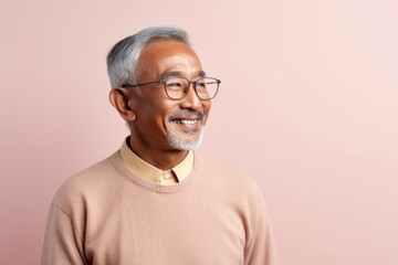 Portrait of a Indonesian man in his 70s in a pastel or soft colors background wearing a chic cardigan
