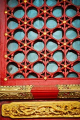ornately carved wood on a red door with glass and brass details