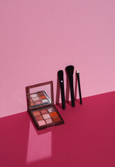 Eye shadow palette with makeup brushes on a pink background with shadow. Creative layout, minimalism