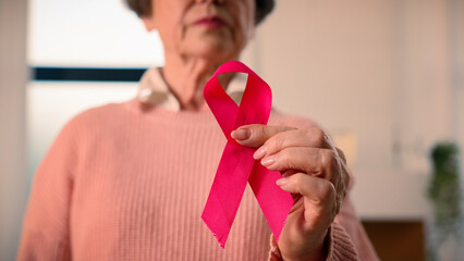 Old senior ill sick woman retired pensioner mature female lady hold red ribbon HIV AIDS awareness...