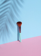 Makeup brush on a pink blue background with palm leaf shadow. Beauty concept. Creative layout, minimalism