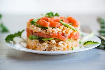 Boiled white rice with salted red fish, cucumbers and other vegetables with herbs in a plate.