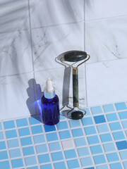 Serum bottle and jade massage roller on tile with palm leaf shadow. Creative layout. Beauty still...